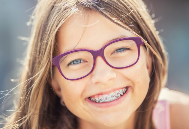 Happy smiling girl with dental braces and glasses. Young cute caucasian blond girl wearing teeth braces and glasses.